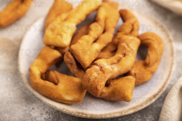 Crunchy biscuit Brushwood cookies sprinkled with powdered sugar on brown concrete background and linen textile, cup of coffee, side view, selective focus