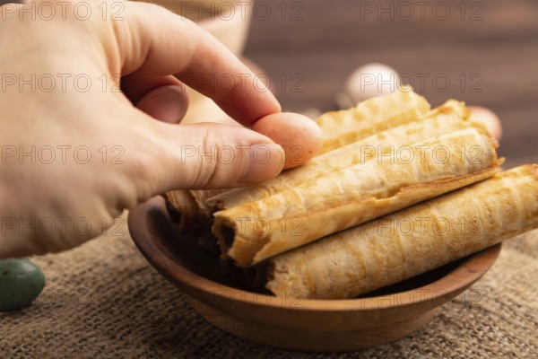 Waffles with caramel with hand on brown wooden background and linen textile, cup of coffee, side view, selective focus