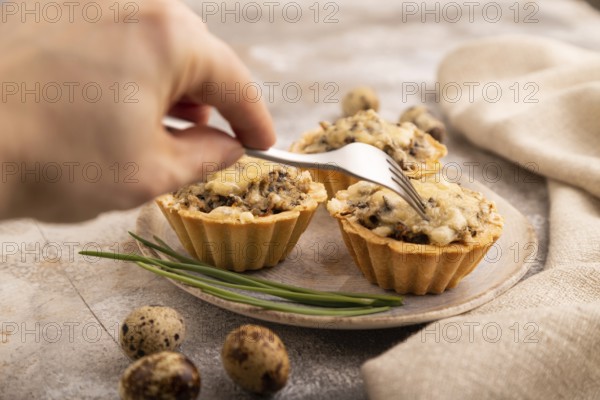 Tartlets with meat and cheese with hand on brown concrete background and linen textile. side view, close up, selective focus