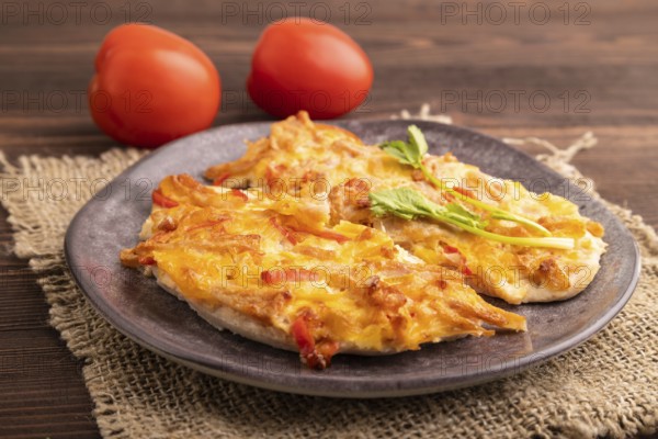 Baked chicken meat with cheese and tomatoes on brown wooden background and linen textile. side view, close up, selective focus