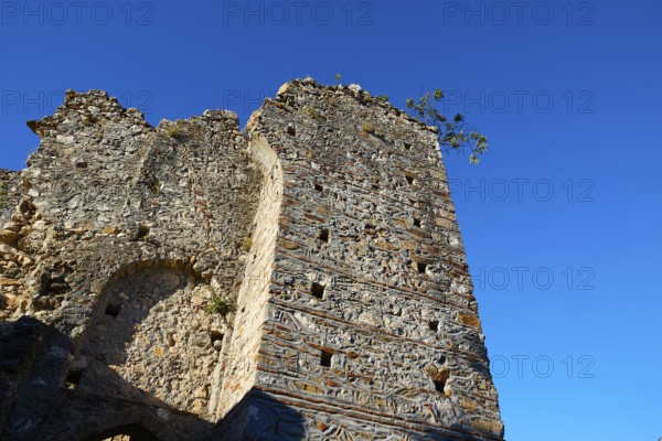 A crumbling stone tower rises under a clear blue sky with few plants, Mystras, Mistra, UNESCO World Heritage Site, Medieval Byzantine ruined city, northwest of Sparta, foothills of the Tyagetos Mountains, Peloponnese, peninsula, Greece