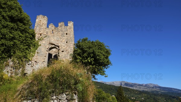 Ancient ruined tower with neighbouring trees against a picturesque blue sky and mountain backdrop, Mystras, Mistra, UNESCO World Heritage Site, Medieval Byzantine ruined city, northwest of Sparta, foothills of the Tyagetos Mountains, Peloponnese, peninsula, Greece
