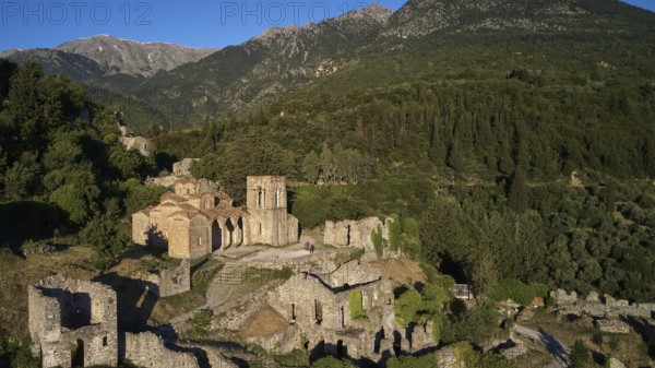Drone shot, Church of Agia Sophia from the 14th century AD, Historic church and ruins with view of forested mountains under blue sky, Mystras, Mistra, UNESCO World Heritage Site, Medieval Byzantine ruined city, northwest of Sparta, foothills of the Tyagetos Mountains, Peloponnese, peninsula, Greece