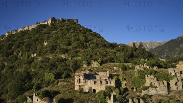 Drone image, Byzantine castle perched on a wooded hill under a blue sky, Mystras, Mistra, UNESCO World Heritage Site, Medieval Byzantine ruined city, northwest of Sparta, foothills of the Tyagetos Mountains, Peloponnese, peninsula, Greece