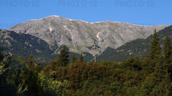 A high mountain rises above dense trees under a bright blue sky, Mystras, Mistra, UNESCO World Heritage Site, Medieval Byzantine ruined city, northwest of Sparta, foothills of the Tyagetos Mountains, Peloponnese, peninsula, Greece
