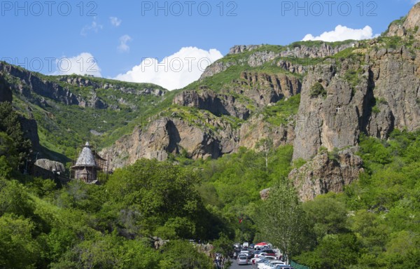 A picturesque gorge with steep rock faces and lush greenery, a church in the background, blue sky and white clouds, Geghard Monastery, UNESCO World Heritage Site, Kotayk Province, Armenia