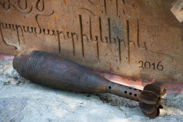 Rusty grenade lies in front of an engraved memorial plaque with the year 2016, mortar shell, memorial site, Shaghap, Ararat province, Armenia