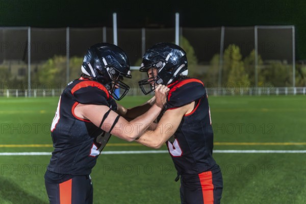 Two american football players in black and orange uniforms collide in a gritty close up on green turf under stadium lights, locked in a physical, high energy struggle