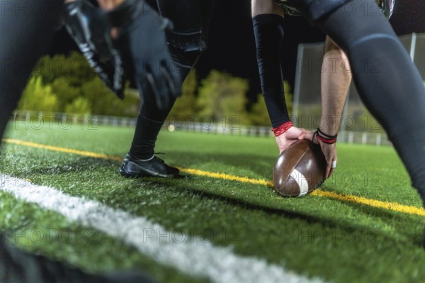 American football player is positioning the leather ball on the marked artificial turf field during a night game, preparing for the kickoff or a key play during competitive sport