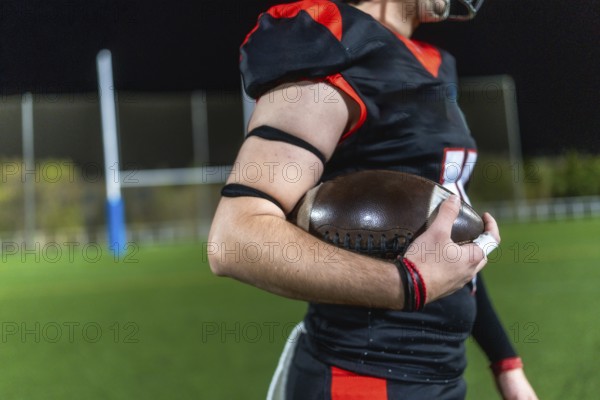 American football player preparing for a game, holding a ball firmly on a sports field lit by stadium lights, representing dedication, strength, and competition