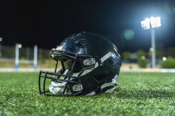 American football helmet lying on green artificial turf field with goal posts and bright stadium lights illuminating the arena at night, representing competition and sports