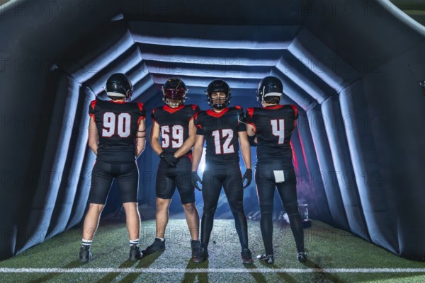 American football team in black uniforms stands inside an inflatable tunnel, helmets on, focused and ready to burst onto the field for a high energy game day showdown