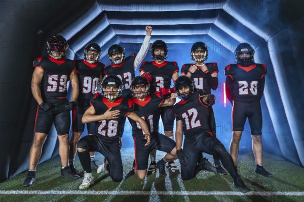 American football team players posing confidently with a victorious gesture, emerging from a stadium tunnel onto the green field with dramatic blue lighting