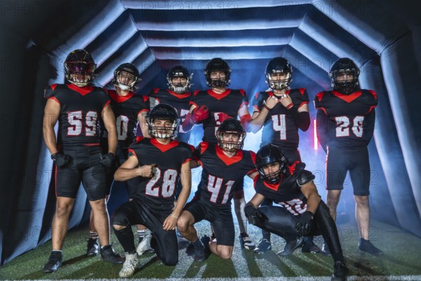 American football team players in uniforms and helmets posing together inside a stadium inflatable tunnel, preparing for a game with determination and confidence