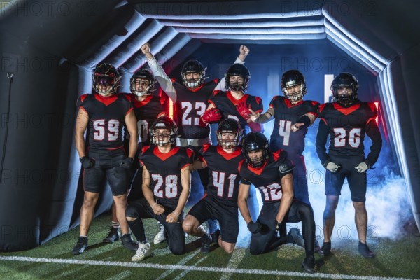 American football team players standing ready to enter the stadium through a tunnel, wearing helmets and black and red uniforms, posing with excitement before the game