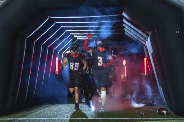 American football players burst from a stadium tunnel into smoke and colored lights, fists raised, sprinting onto the field in a show of determination, energy, and victory anticipation