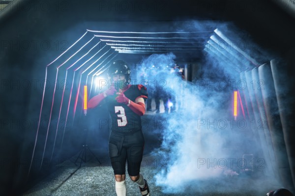 American football player in uniform and helmet emerging from a stadium tunnel filled with smoke and dramatic lighting, expressing determination before a game