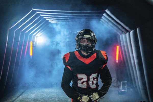 American football player in uniform and helmet emerges from a fog filled stadium tunnel into dramatic spotlight, ready and focused to take the field for the big game