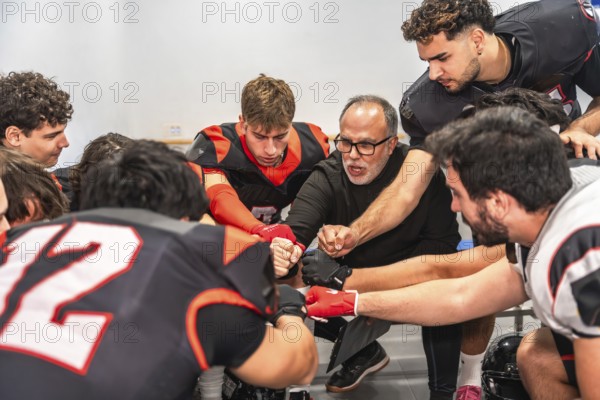 American football coach and players huddling in a locker room, getting motivated for a game while placing their fists together in a gesture of unity and teamwork