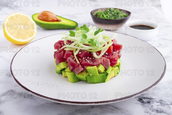 Fresh tuna tartare with avocado served on a marble table with soy sauce and seaweed salad