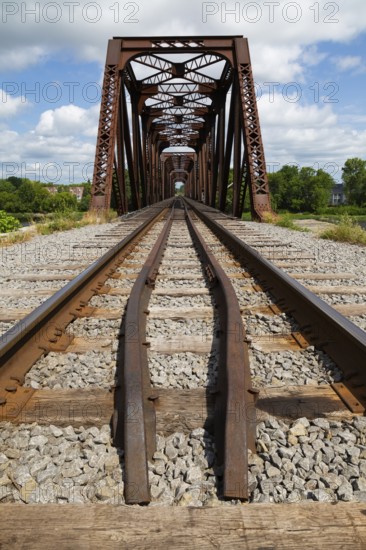 Railroad tracks leading to old rusted Terrebonne Pratt truss railroad bridge over Des Mille-Iles river in summer, Laval, Quebec, Canada