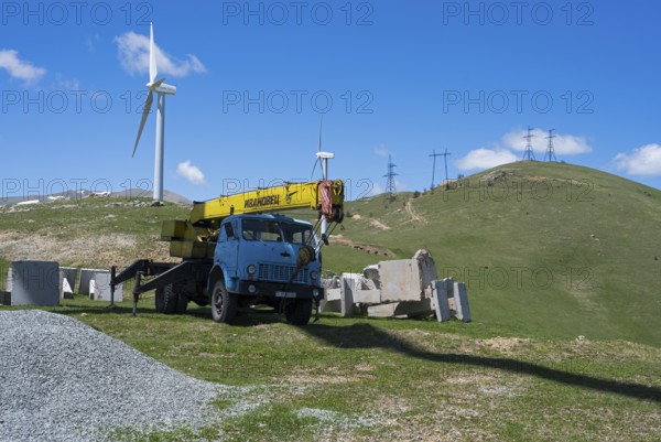 A blue crane lorry stands on a green construction site next to a wind turbine on a hill, Pushkin Pass, Lorikeet Province, Bazum Mountains, Lesser Caucasus, Armenia