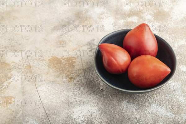 Red Heart shape tomatoes in blue bowl on brown concrete background. Side view, copy space. healthy food, vegetable, minimalism