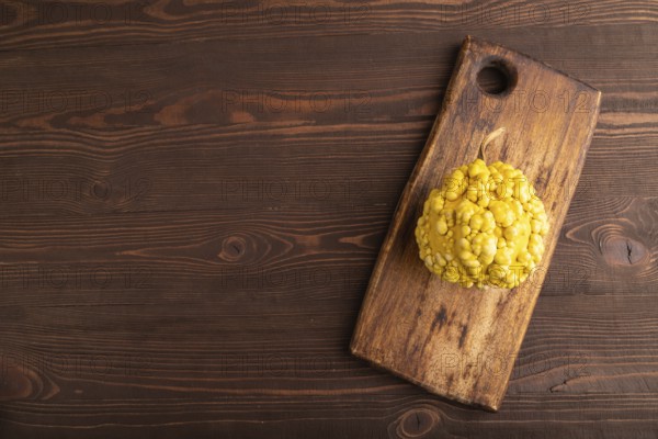 Decorative orange Pumpkin with tumors on cutting board on brown wooden background, top view, flat lay, copy space, minimalism