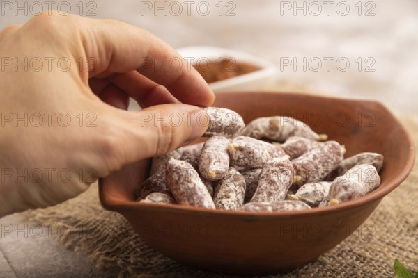 Small smoked Chicken sausages in clay bowl with hand on brown concrete background and linen textile. side view, close up, selective focus
