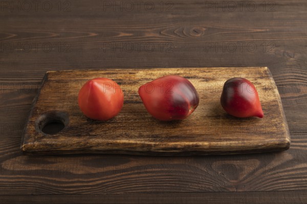 Red Heart shape tomatoes on cutting board on brown wooden background. Side view, copy space. healthy food, vegetable, minimalism