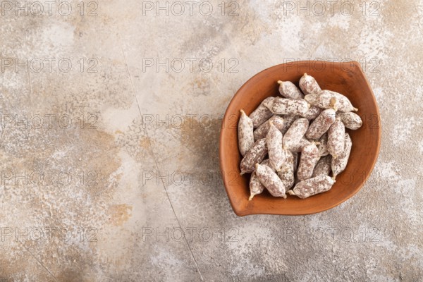 Small smoked Chicken sausages in clay bowl on brown concrete background. top view, copy space
