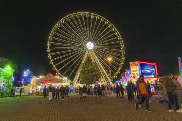 Large Ferris wheel lights up the night while people visit the stalls, Cannstatter Wasen folk festival, Stuttgart, Germany