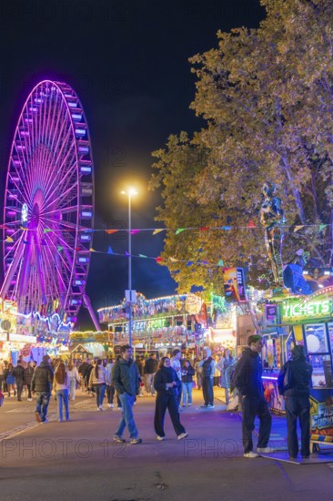 Festive atmosphere with fairy lights and a large Ferris wheel at night, Cannstatter Wasen folk festival, Stuttgart, Germany
