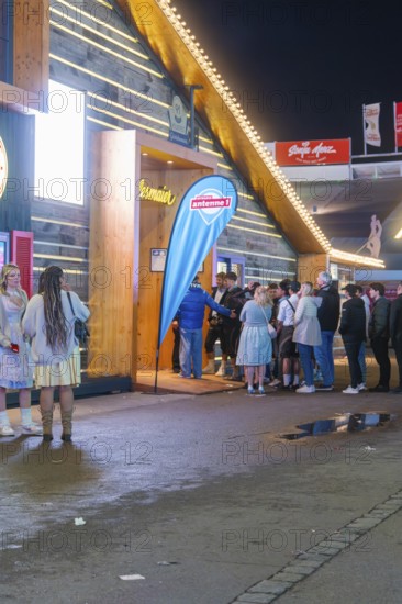 People standing in front of an illuminated marquee at night while waiting for admission, Cannstatter Wasen folk festival, Stuttgart, Germany