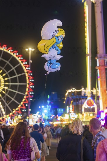 View of a Smurf balloon floating between a crowd at a funfair, with Ferris wheel in the background, Cannstatter Wasen funfair, Stuttgart, Germany