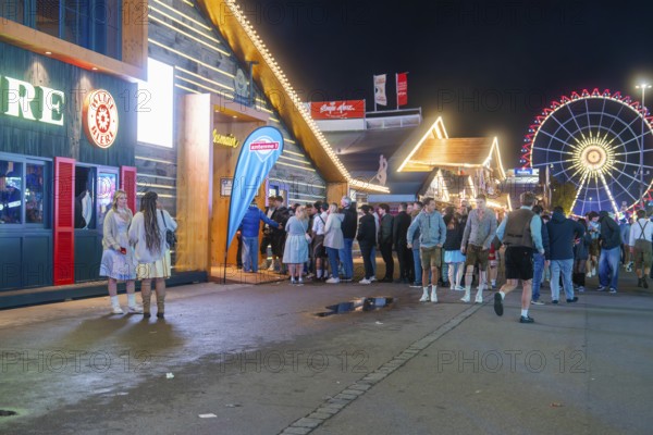 Crowd in front of illuminated festival tents and a large Ferris wheel at night, Cannstatter Wasen folk festival, Stuttgart, Germany