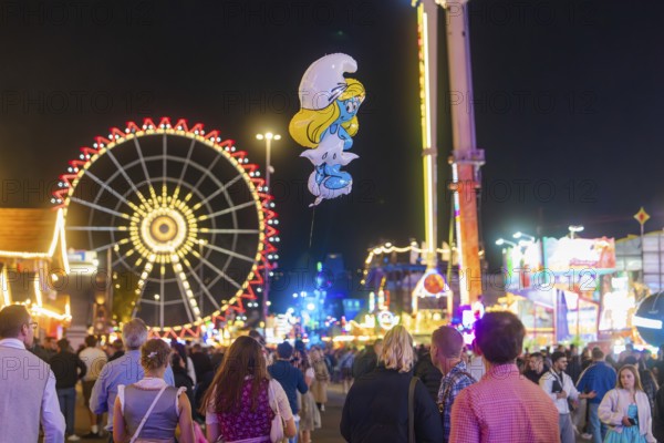 People enjoying the hustle and bustle of a fairground at night with a large Ferris wheel in the background, Cannstatter Wasen fairground, Stuttgart, Germany