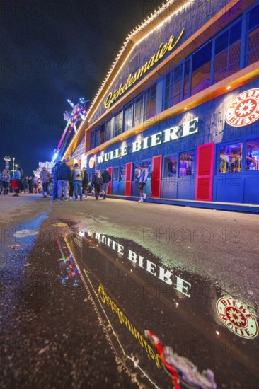 Reflection of the colourful lights of a beer hall on a wet street at night, Cannstatter Wasen folk festival, Stuttgart, Germany