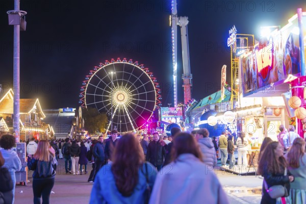 Lively funfair at night with lots of people and a large, illuminated Ferris wheel, Cannstatter Wasen funfair, Stuttgart, Germany