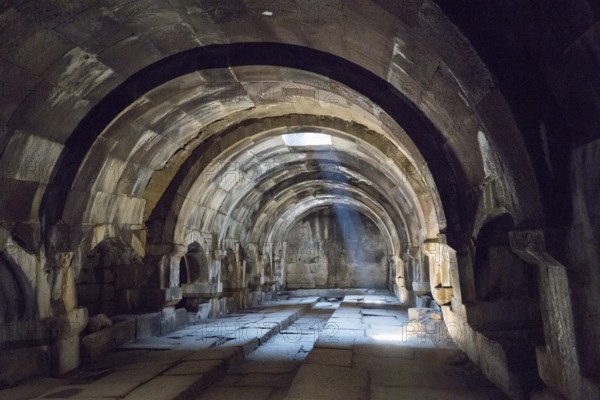 Interior view of an ancient vault with stone arches and a beam of light creating a mysterious atmosphere, Orbelian's Caravanserai, Selim Caravanserai, located at the Vardenyats Pass or Selim Pass, Vayots Dzor Province, Armenia