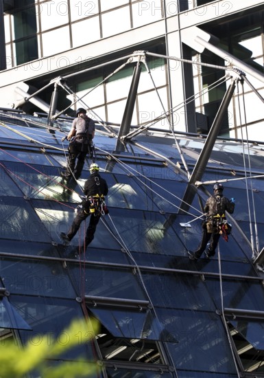 Three male glass cleaners abseiling down a glass roof of Berlin Central Station to clean windows, Berlin, Germany