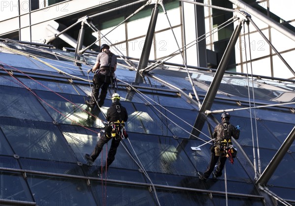 Three male glass cleaners abseiling down a glass roof of Berlin Central Station to clean windows, Berlin, Germany