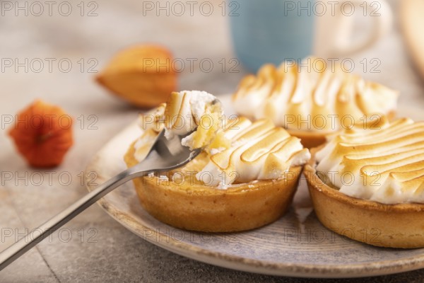 French lemon tart with meringue on brown concrete background, cup of coffee, orange linen textile, side view, close up, selective focus