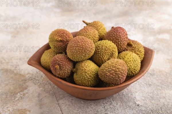 Ripe Lychee on clay bowl on brown concrete background, side view, close up, minimalism