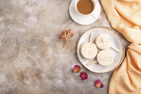 ?hocolate Ice cream in white glaze, cup of coffee, on brown concrete background and orange textile, top view, flat lay, copy space, minimalism