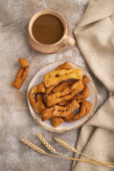 Crunchy biscuit Brushwood cookies sprinkled with powdered sugar on brown concrete background and linen textile, cup of coffee, top view, flat lay, close up