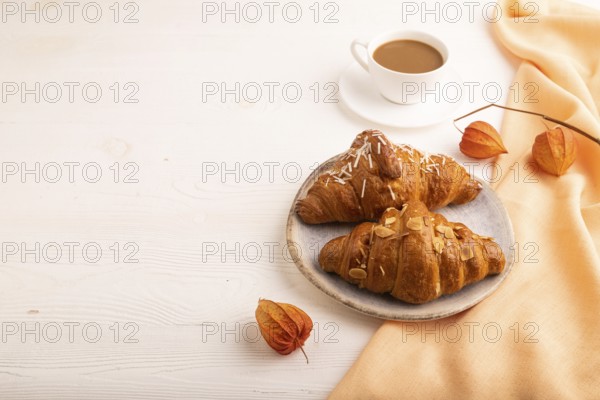 Croissant on blue plate on white wooden background and orange linen textile, cup of coffee, side view, copy space