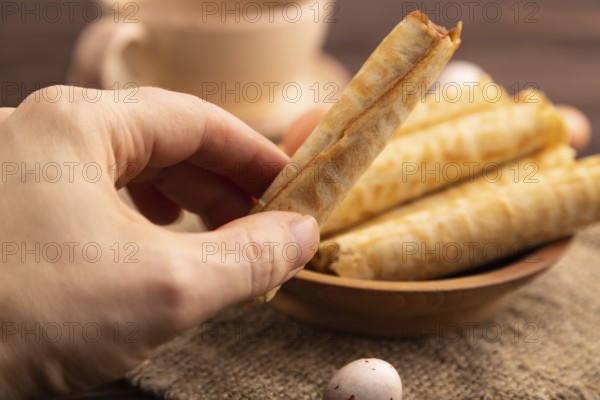 Waffles with caramel with hand on brown wooden background and linen textile, cup of coffee, side view, selective focus