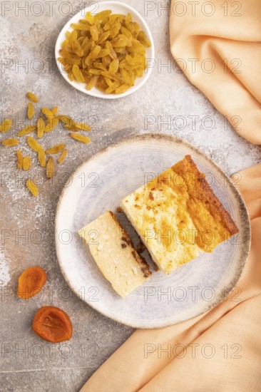 ?ottage cheese ?asserole, Curd cake, with dried apricots and raisins on brown concrete background and orange textile, top view, flat lay, close up, minimalism