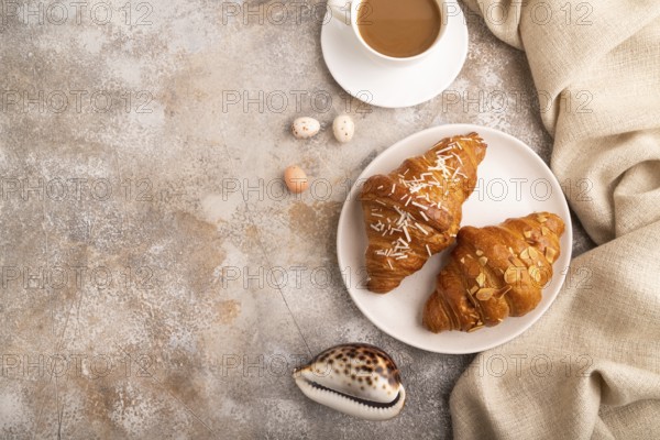 Croissant on white plate on brown concrete background and linen textile, cup of coffee, top view, flat lay, copy space